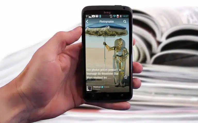 quelqu'un tenant un téléphone intelligent dans la main avec un magazine en arrière-plan