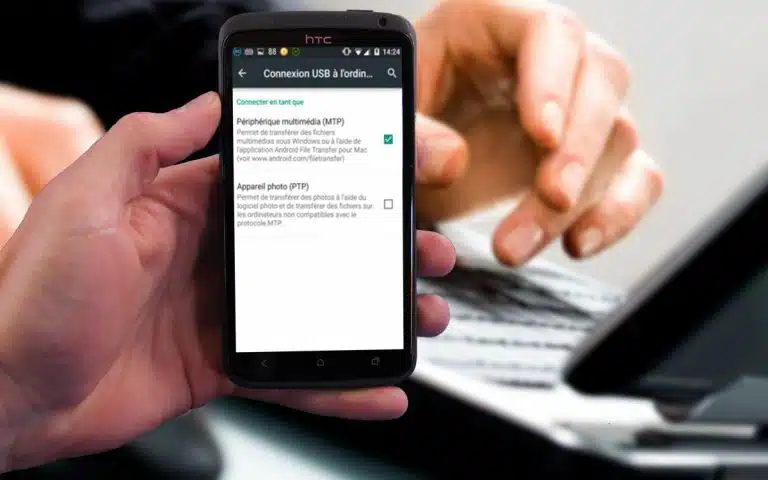 quelqu'un tenant un téléphone intelligent dans sa main avec un ordinateur portable en arrière-plan